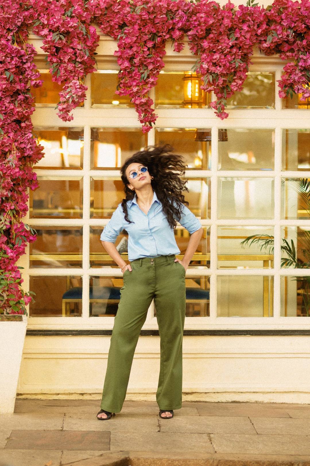 A woman in a blue shirt and olive trousers under bougainvillea