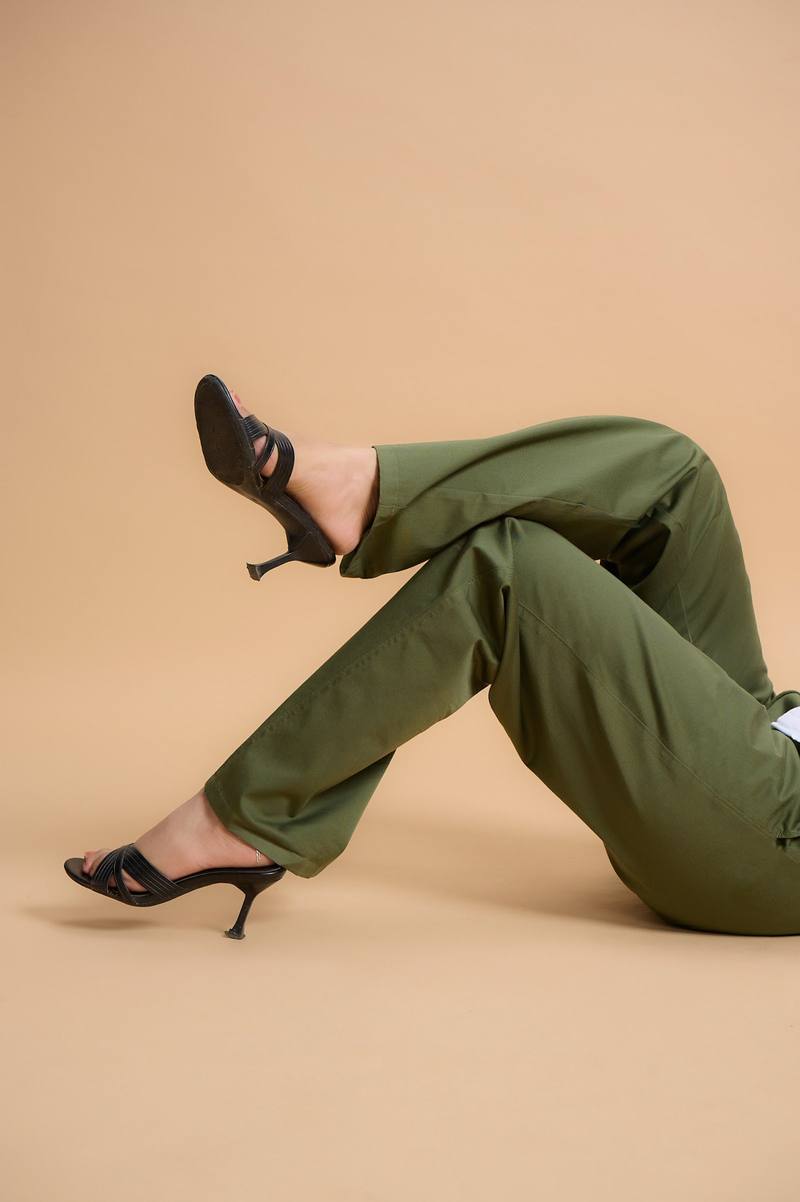 Legs in olive trousers and black heels against a tan backdrop
