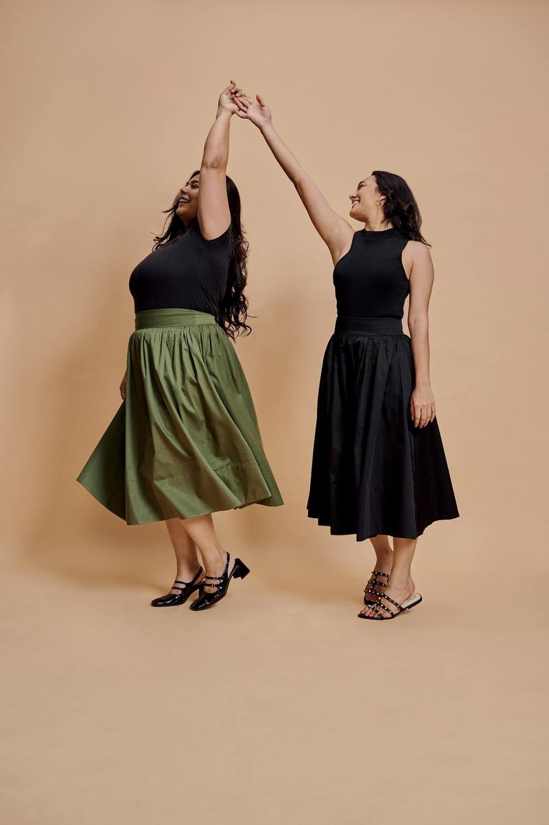 Two women dancing in olive and black skirts in the studio