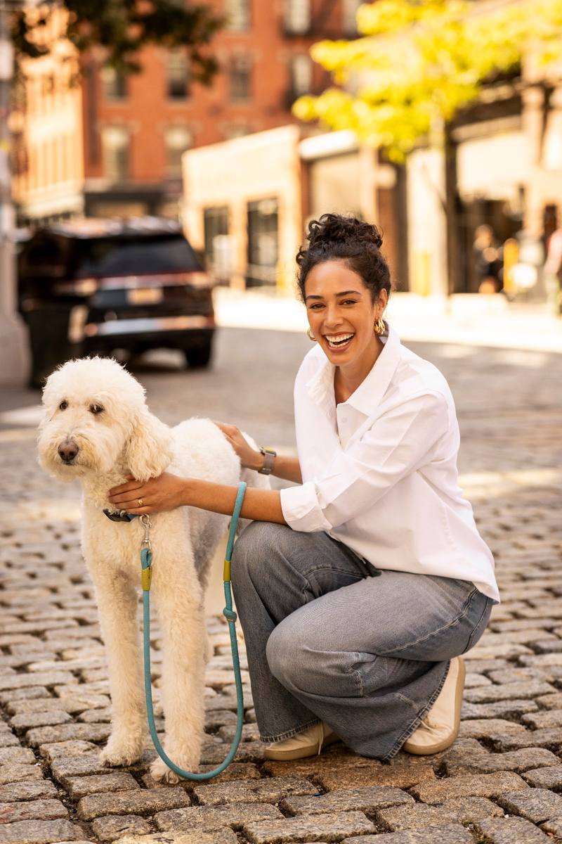 A woman in a white shirt crouching beside a poodle on a cobbled street
