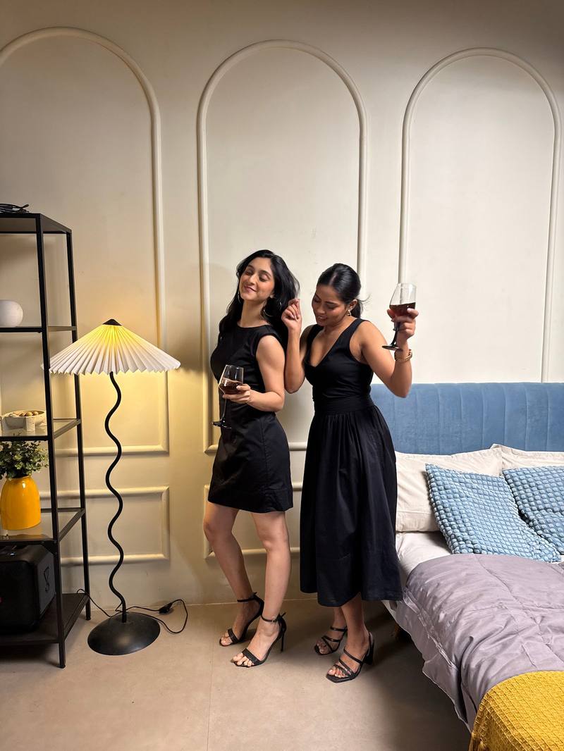 Two friends laughing at home, one in the Little Black Dress, one in the black Do-It-All Skirt